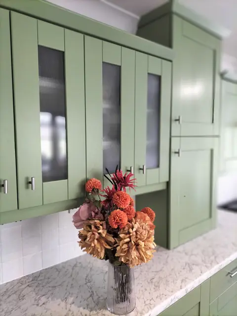 Sage green glazed wall cabinets above a granite worktop