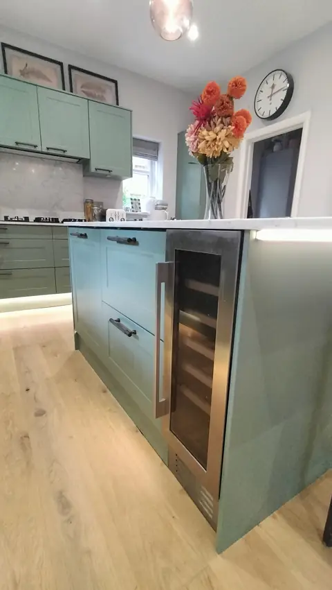 Sage green island with wine fridge on an oak floor